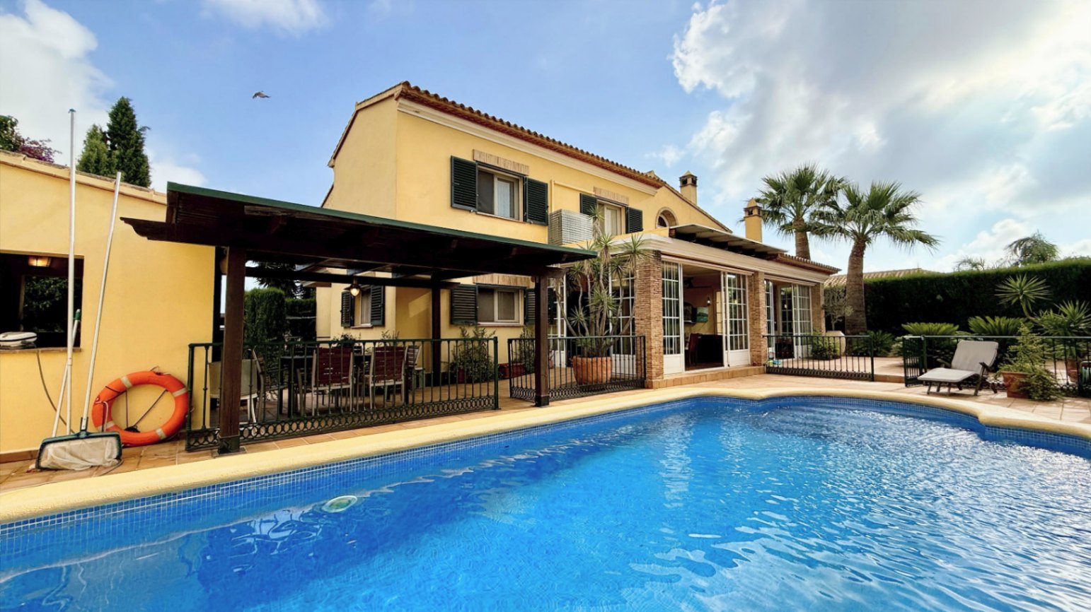 Ruim villa met zwembad, grote kelder en maximale privacy in Dénia Gelegen in een van de rustigste woonwijken van Dénia, combineert deze prachtige villa privacy, ruimte en een uitstekende verbinding met het stadscentrum. Gebouwd op een perceel van 811 m², omgeven door groen, biedt het een verzorgde en besloten omgeving, ideaal om te genieten van de rust zonder in te boeten op alle voorzieningen. De woning beschikt over vier slaapkamers, verdeeld over twee verdiepingen, en ruime, lichte ruimtes die zijn ontworpen voor dagelijks comfort. De keuken, van royale afmetingen, functioneert ook als eetkamer en ontvangt veel natuurlijk licht dankzij de grote ramen. Op de bovenverdieping bevindt zich een aparte kantoorruimte en de hoofdsuite, die beschikt over een eigen badkamer, inloopkast en balkon. Buiten steekt een mooie tuin met eigen bronirrigatie, een zwembad van 9 x 5 meter dat perfect in de omgeving is geïntegreerd, een zomerkeuken en een ruime glazen veranda met open haard, perfect om het hele jaar door van te genieten. De woning beschikt ook over een overdekte garage en ruime buitenruimtes. Een van de grootste aantrekkingskrachten van deze villa is de grote kelder die volledig is ingericht, droog en met uitstekende natuurlijke ventilatie, een zeer veelzijdige ruimte die momenteel een fitnessruimte, speelruimte en biljart bevat, en bovendien de mogelijkheid biedt om een sauna te installeren. De woning is uitgerust met airconditioning in de woonkamer en slaapkamers, een fotovoltaïsche installatie van meer dan 6 kW, alarmsysteem, veiligheidssloten, ramen met inbraakbescherming in verschillende ruimtes, horren, aparte wasruimte, osmosewater in de keuken, een olieopslag van 1.000 liter, aansluiting op het riolering en een compleet drainsysteem dat de kelder beschermt tegen vocht. Een eigendom van uitstekende constructkwaliteit, met ruime binnen- en buitenruimtes, ideaal als permanente woning of om het hele jaar van de Costa Blanca te genieten.