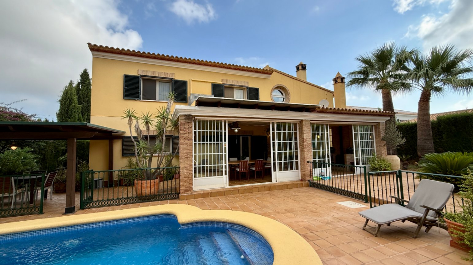 Ruim villa met zwembad, grote kelder en maximale privacy in Dénia Gelegen in een van de rustigste woonwijken van Dénia, combineert deze prachtige villa privacy, ruimte en een uitstekende verbinding met het stadscentrum. Gebouwd op een perceel van 811 m², omgeven door groen, biedt het een verzorgde en besloten omgeving, ideaal om te genieten van de rust zonder in te boeten op alle voorzieningen. De woning beschikt over vier slaapkamers, verdeeld over twee verdiepingen, en ruime, lichte ruimtes die zijn ontworpen voor dagelijks comfort. De keuken, van royale afmetingen, functioneert ook als eetkamer en ontvangt veel natuurlijk licht dankzij de grote ramen. Op de bovenverdieping bevindt zich een aparte kantoorruimte en de hoofdsuite, die beschikt over een eigen badkamer, inloopkast en balkon. Buiten steekt een mooie tuin met eigen bronirrigatie, een zwembad van 9 x 5 meter dat perfect in de omgeving is geïntegreerd, een zomerkeuken en een ruime glazen veranda met open haard, perfect om het hele jaar door van te genieten. De woning beschikt ook over een overdekte garage en ruime buitenruimtes. Een van de grootste aantrekkingskrachten van deze villa is de grote kelder die volledig is ingericht, droog en met uitstekende natuurlijke ventilatie, een zeer veelzijdige ruimte die momenteel een fitnessruimte, speelruimte en biljart bevat, en bovendien de mogelijkheid biedt om een sauna te installeren. De woning is uitgerust met airconditioning in de woonkamer en slaapkamers, een fotovoltaïsche installatie van meer dan 6 kW, alarmsysteem, veiligheidssloten, ramen met inbraakbescherming in verschillende ruimtes, horren, aparte wasruimte, osmosewater in de keuken, een olieopslag van 1.000 liter, aansluiting op het riolering en een compleet drainsysteem dat de kelder beschermt tegen vocht. Een eigendom van uitstekende constructkwaliteit, met ruime binnen- en buitenruimtes, ideaal als permanente woning of om het hele jaar van de Costa Blanca te genieten.
